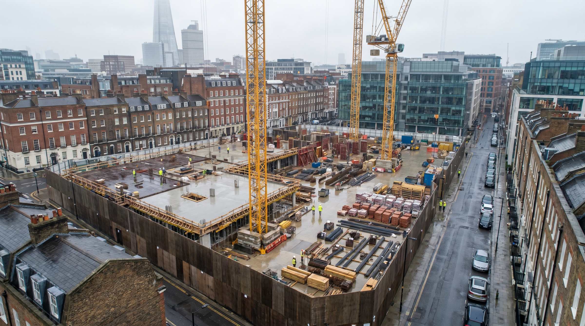 Aerial drone view looking down over an active Central London construction site with tower cranes and the surrounding cityscape
