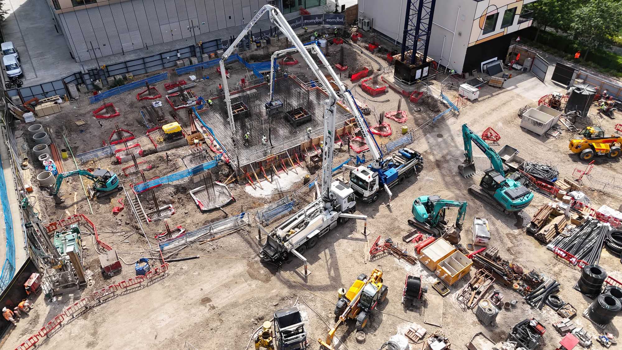 Aerial view of an active Central London construction site during a concrete pour, with rebar mat, concrete pump, and excavators